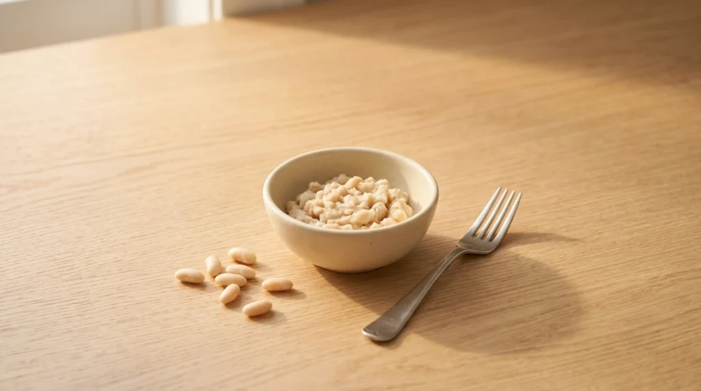 A small bowl of mashed white beans next to a fork and whole beans on a wooden table, demonstrating the thickening secret for creamy white chicken chili.