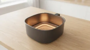 An empty basket-style air fryer sits on a wooden kitchen counter, staged for preheating to create the ideal environment for cooking a juicy air fryer chicken breast. To ensure the best results, preheat your air fryer to 375°F for 3 minutes before adding your seasoned chicken. This quick and essential preheating step sets the stage for evenly cooked, tender, and succulent chicken, making your home-cooked meal taste like it came straight from a professional kitchen.