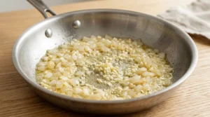 Diced onions and minced garlic saute in melted butter within a stainless steel skillet, creating the flavorful aromatic base for your one pan chicken and rice dinner. To prepare, reduce the skillet heat to medium, add the butter, and cook the diced onions for three minutes until softened. Finally, add the minced garlic and stir for 45 seconds until fragrant, perfectly prepping the pan to incorporate the remaining ingredients for this simple, delicious home cooked meal.