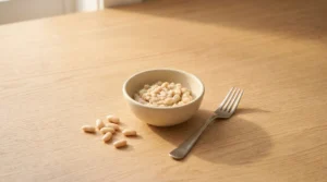 A small bowl of mashed white beans next to a fork and whole beans on a wooden table, demonstrating the thickening secret for creamy white chicken chili.