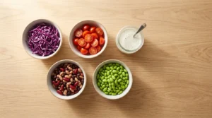 Fresh vegetables, beans, and edamame being prepared on a light wood countertop, ready for high protein chicken bowl meal prep.