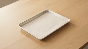 A clean, metal half-sheet pan lined with parchment paper, sitting on a light wood grain table, ready for preparing chicken and butternut squash.