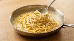 A bowl of creamy fettuccine topped with sliced chicken and fresh parsley, prepared for a chicken alfredo recipe.