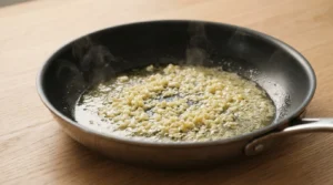Minced garlic cooking in melted butter in a skillet until fragrant, prepared for a chicken alfredo recipe.