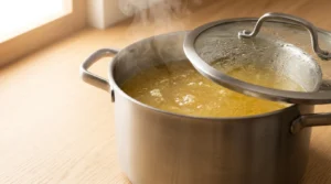 A pot of soup simmering gently on low heat with the lid slightly ajar, prepared for chicken soup recipe.