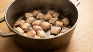 Chicken pieces searing in a large pot over medium-high heat until lightly browned, prepared for chicken curry from scratch.